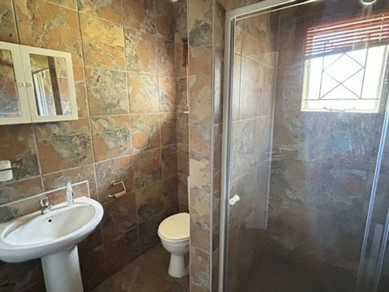 A functional bathroom featuring a pedestal basin, toilet, and a glass-enclosed shower, finished with full-height wall tiling.