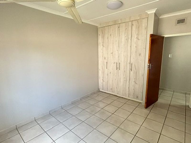 An empty bedroom featuring light-toned built-in cupboards, tiled flooring, and a ceiling fan, offering a clean and neutral space ready for personalization.