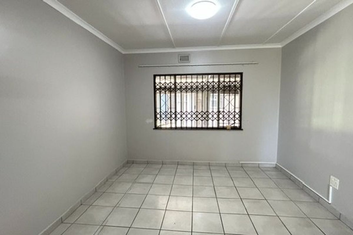 A clean, empty bedroom featuring neutral wall paint, tiled flooring, and security bars on the window.