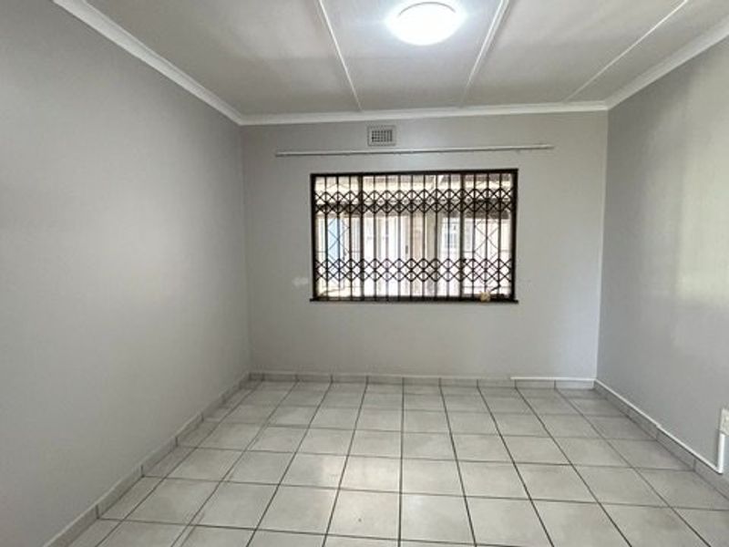 A clean, empty bedroom featuring neutral wall paint, tiled flooring, and security bars on the window.