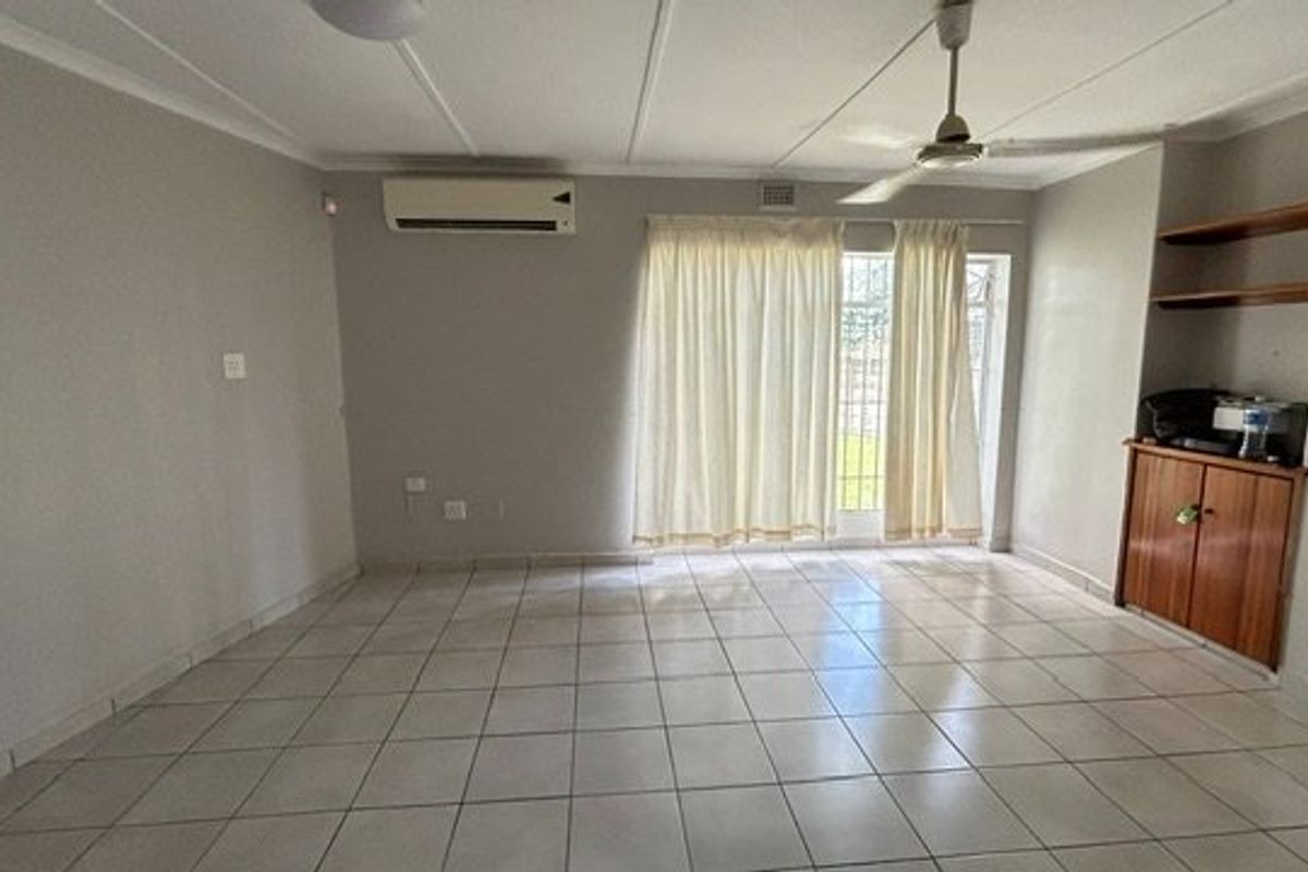 Spacious living area featuring neutral tiled flooring, a ceiling fan, split-system air conditioning, and built-in storage cabinetry with shelving.