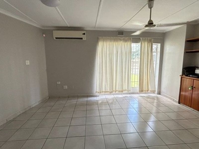 Spacious living area featuring neutral tiled flooring, a ceiling fan, split-system air conditioning, and built-in storage cabinetry with shelving.