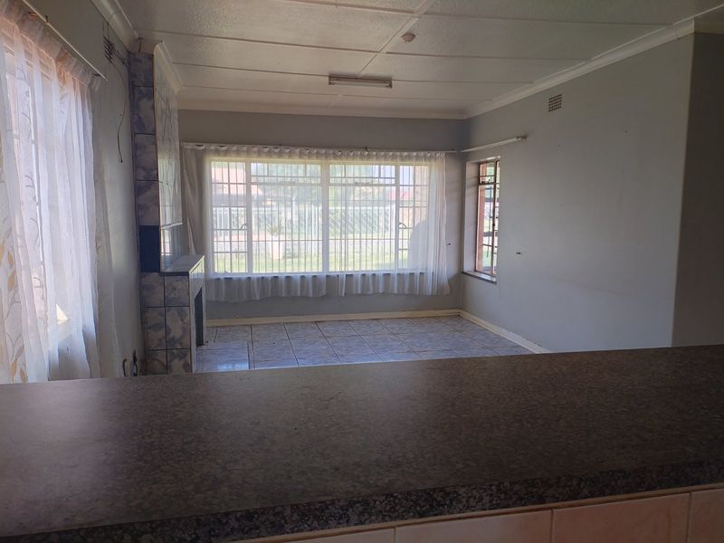 Open plan living area featuring tiled flooring, a built-in tiled fireplace, and a breakfast counter overlooking the space with large windows and security bars.