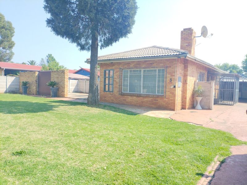A single-story face brick house featuring a tiled roof, chimney, and security bars, set on a property with a lawn and paved driveway.