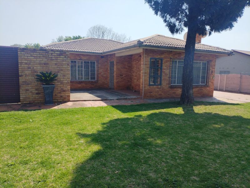 A single-story face brick house featuring a tiled roof, security bars on windows, and a front concrete patio set within a grassed yard.