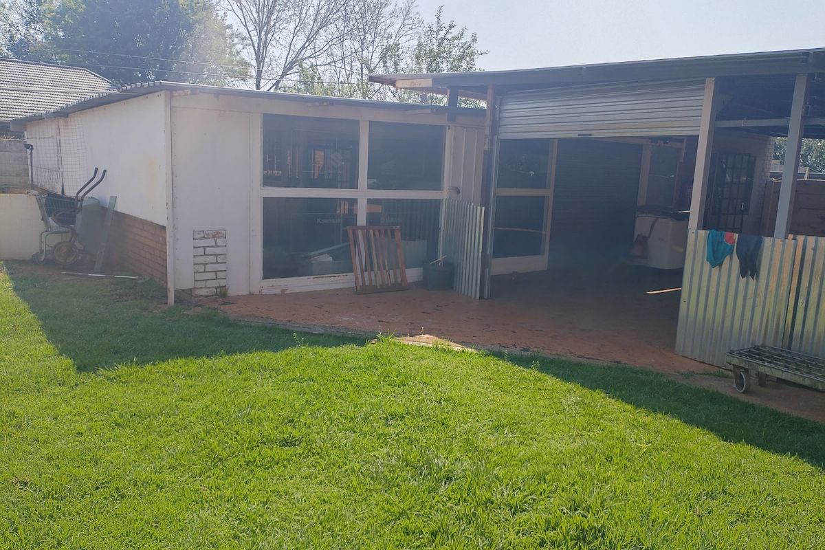 Rear view of the property showing a detached structure with a roller shutter door, brick and metal construction, and an adjacent lawn area.
