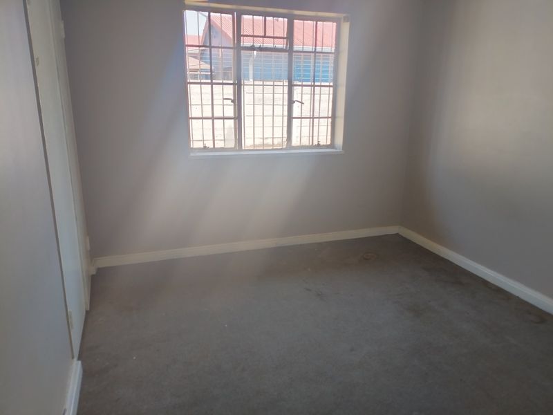 An empty bedroom featuring carpeted flooring, neutral walls, and a window fitted with security burglar bars.