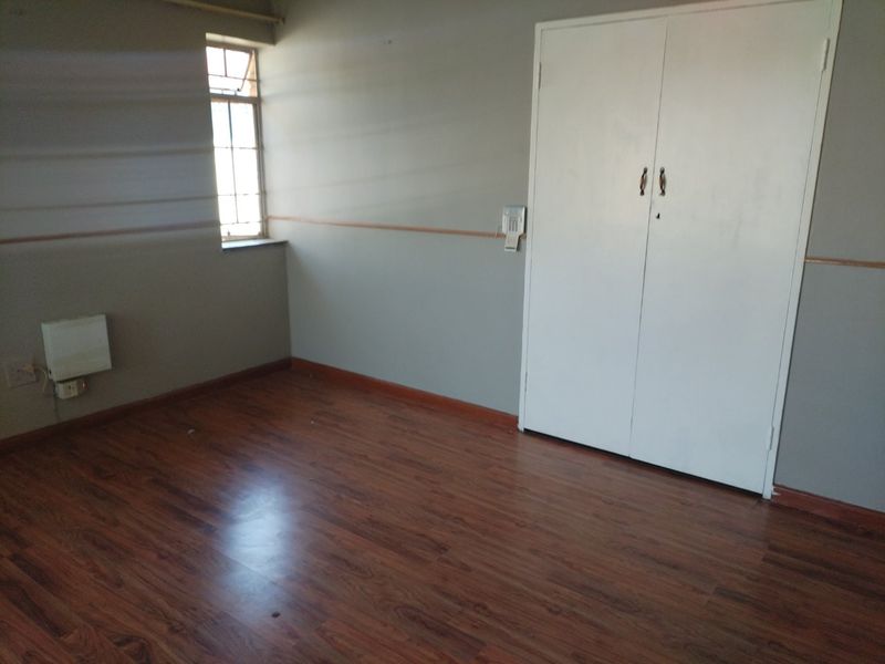 An empty bedroom featuring laminate flooring, a built-in wardrobe, and a wall-mounted heater, offering a blank canvas for personalization.