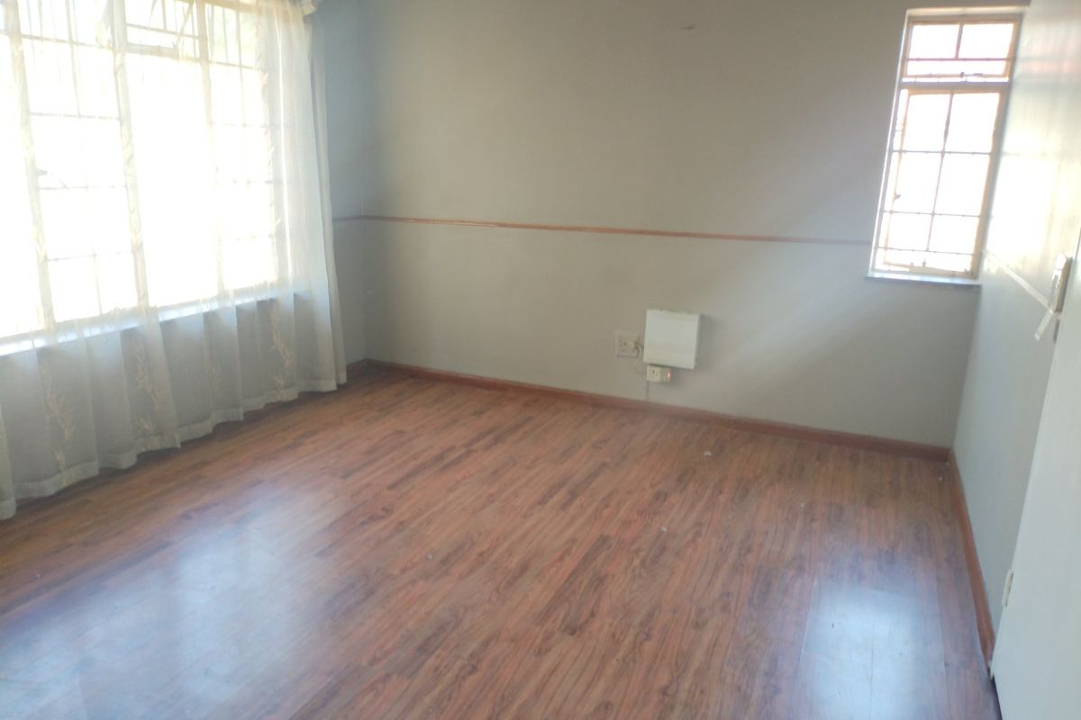 An empty bedroom featuring laminate flooring, a timber dado rail, and natural light from steel frame windows.