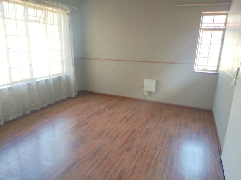 An empty bedroom featuring laminate flooring, a timber dado rail, and natural light from steel frame windows.