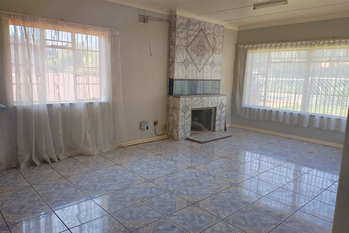 Spacious living room featuring tiled flooring, a central tiled fireplace, and large windows with security bars, offering a blank canvas for renovation.