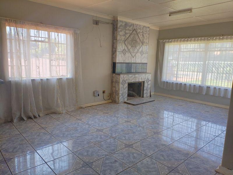 Spacious living room featuring tiled flooring, a central tiled fireplace, and large windows with security bars, offering a blank canvas for renovation.