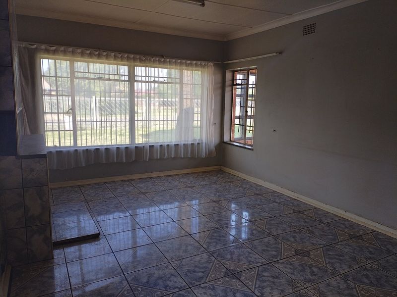 An empty living room featuring tiled flooring, security bars on the windows, and a tiled fireplace hearth.