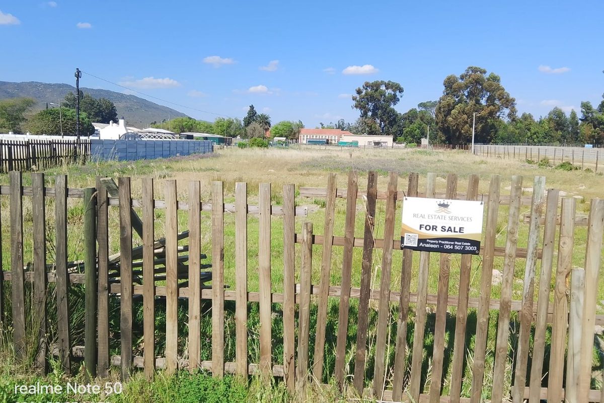 A vacant residential plot enclosed by a wooden picket fence, featuring a for sale sign and clear views of the surrounding landscape.