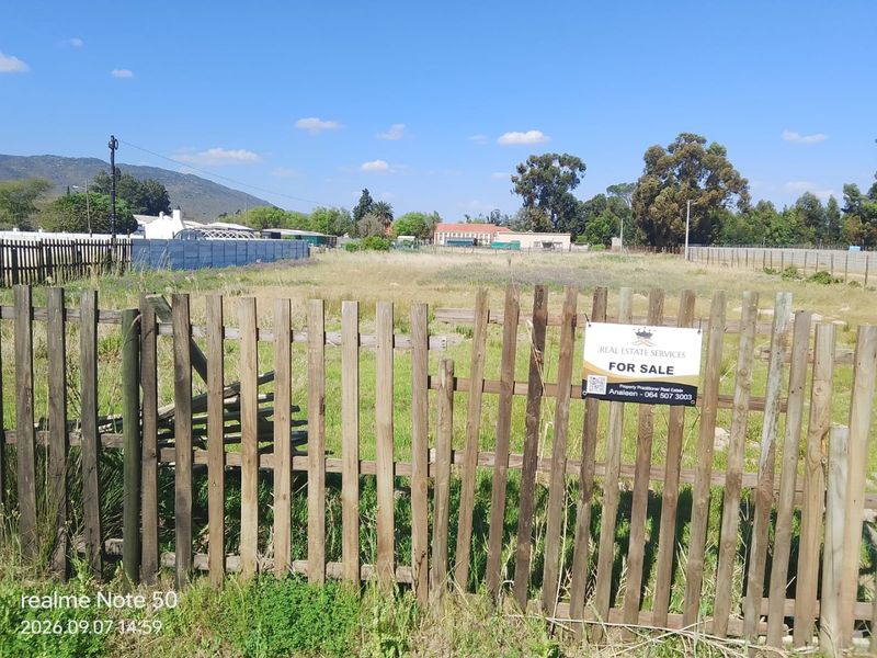 A vacant residential plot enclosed by a wooden picket fence, featuring a for sale sign and clear views of the surrounding landscape.
