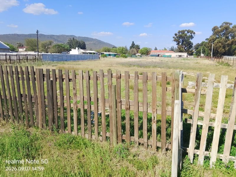 A view of a vacant residential plot featuring a weathered wooden picket fence boundary.