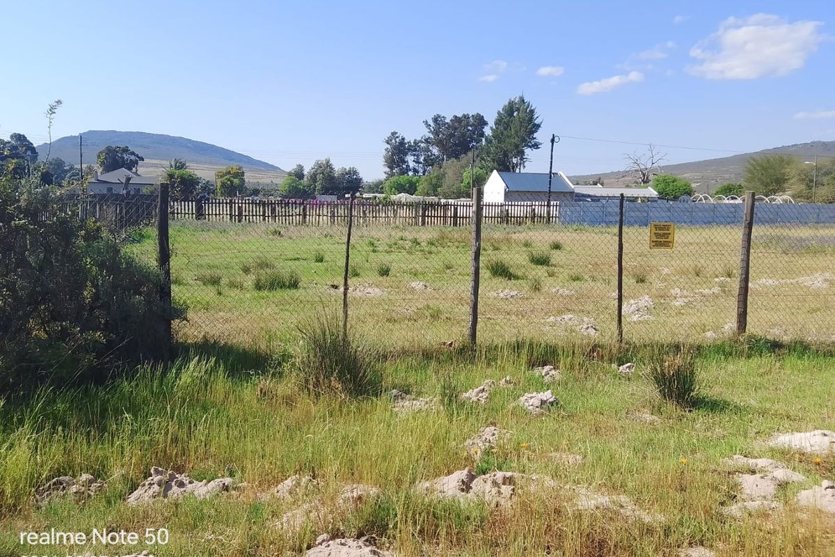 A vacant residential plot featuring natural grass coverage and perimeter wire mesh fencing with wooden posts.