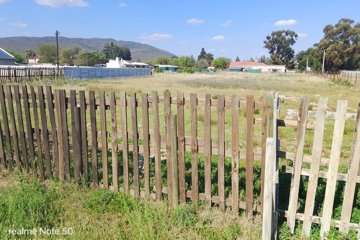 A view of a vacant residential plot featuring a weathered wooden picket fence boundary.