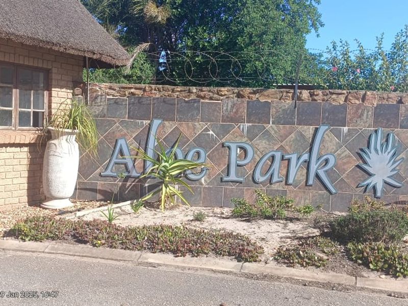 Entrance view of Aloe Park featuring a brick guardhouse with a thatched roof and stone boundary wall with security fencing.