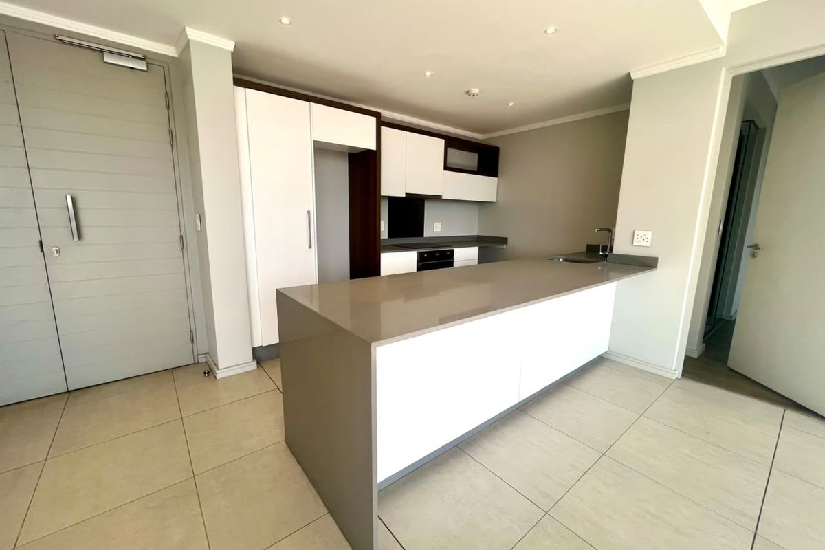 Modern open-plan kitchen featuring a large island with quartz countertops, built-in oven, extractor fan, and sleek white and dark cabinetry.
