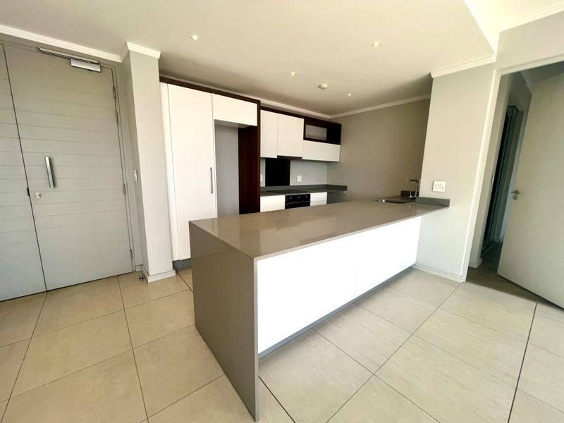 Modern open-plan kitchen featuring a large island with quartz countertops, built-in oven, extractor fan, and sleek white and dark cabinetry.