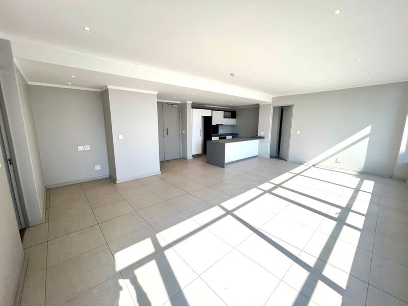 Spacious open-plan living area featuring neutral tiled flooring, recessed lighting, and a modern kitchen with a central island and built-in cabinetry.