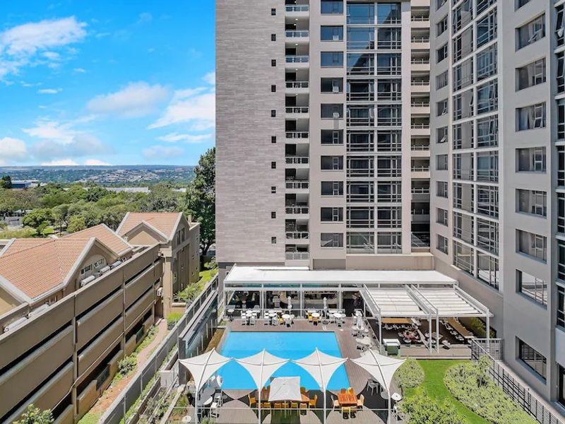 Elevated view of a modern apartment complex featuring a swimming pool, timber decking, shaded outdoor seating areas, and landscaped garden space.