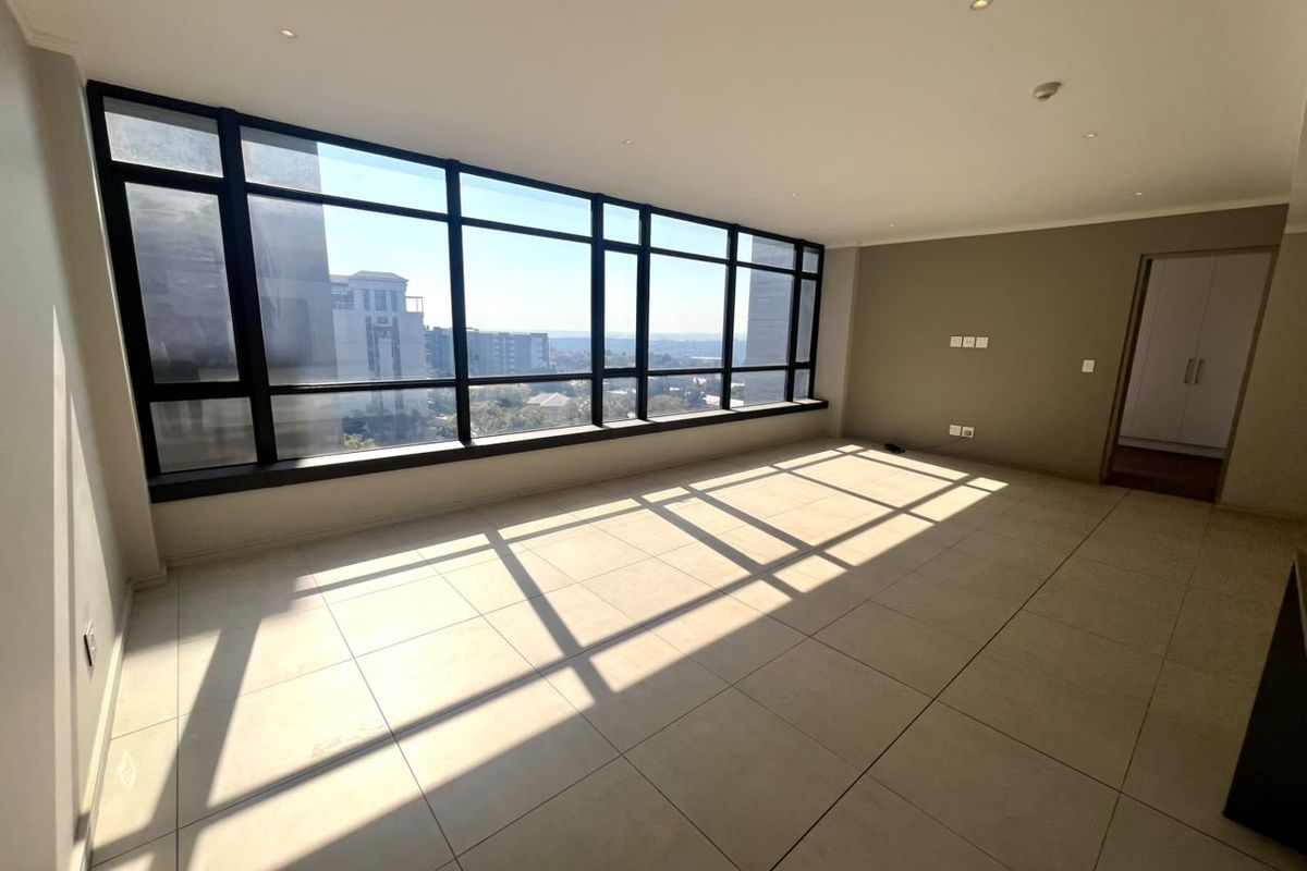 Spacious, sunlit living area featuring large floor-to-ceiling windows with expansive views, neutral tiled flooring, and recessed lighting in a modern apartment setting.