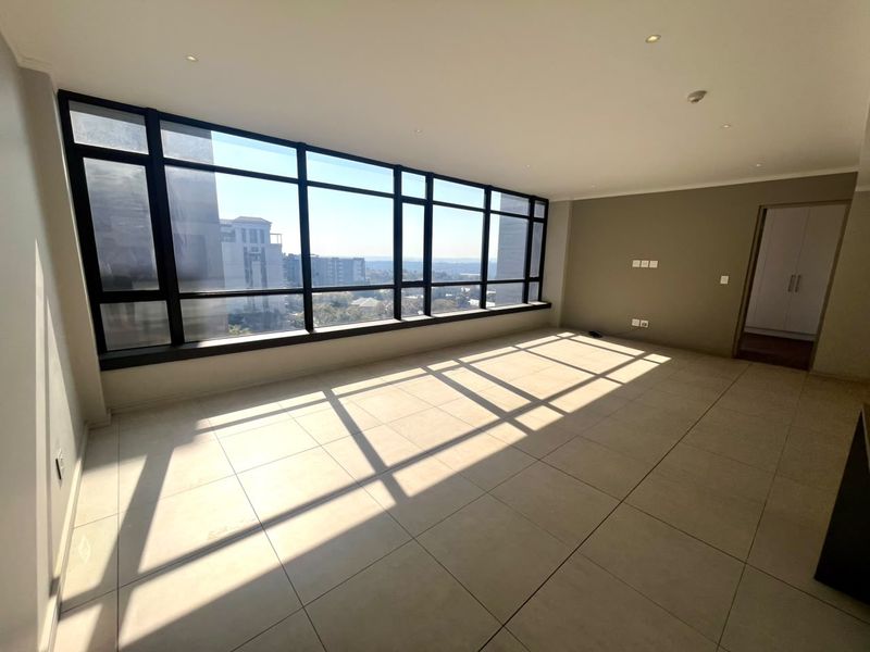 Spacious, sunlit living area featuring large floor-to-ceiling windows with expansive views, neutral tiled flooring, and recessed lighting in a modern apartment setting.