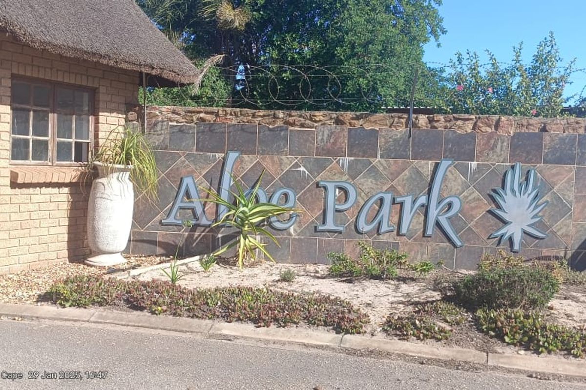 Entrance view of Aloe Park featuring a brick guardhouse with a thatched roof and stone boundary wall with security fencing.