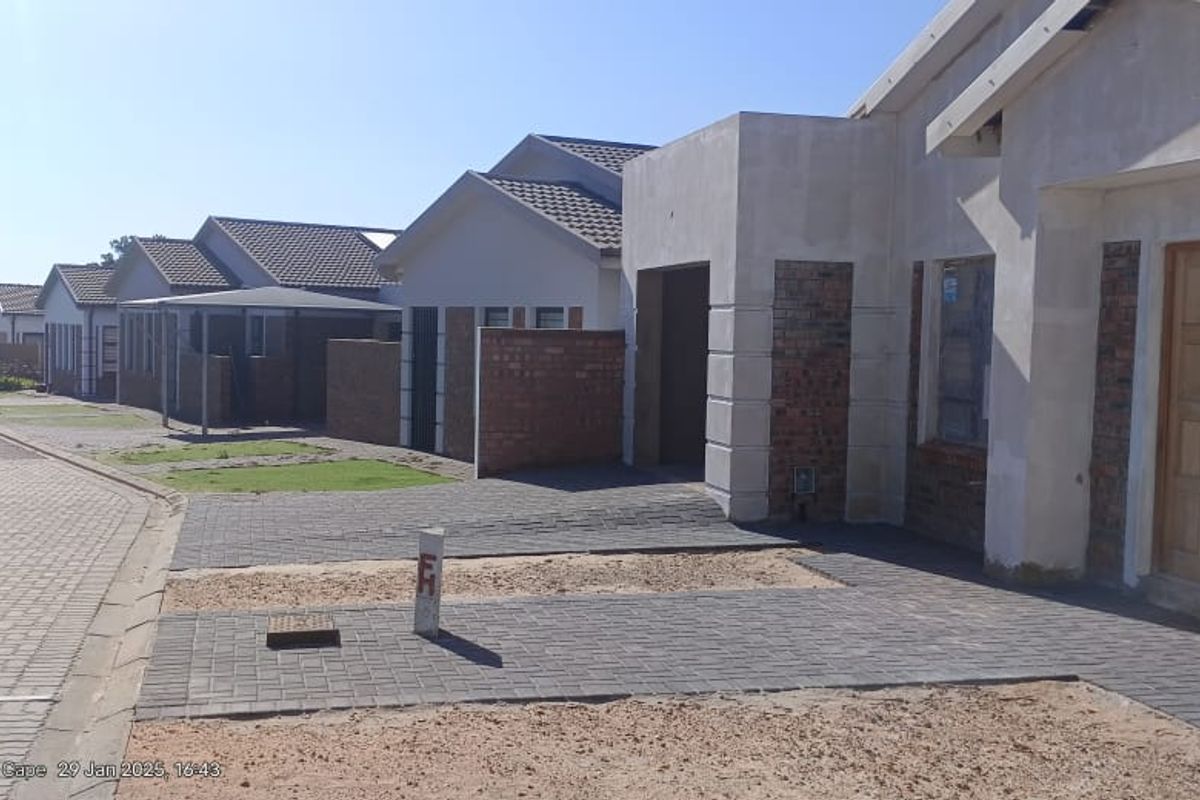A street view of a residential development featuring newly constructed houses with paved driveways and brick and plaster facades.