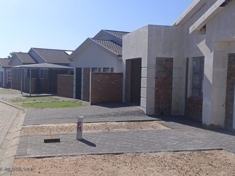 A street view of a residential development featuring newly constructed houses with paved driveways and brick and plaster facades.