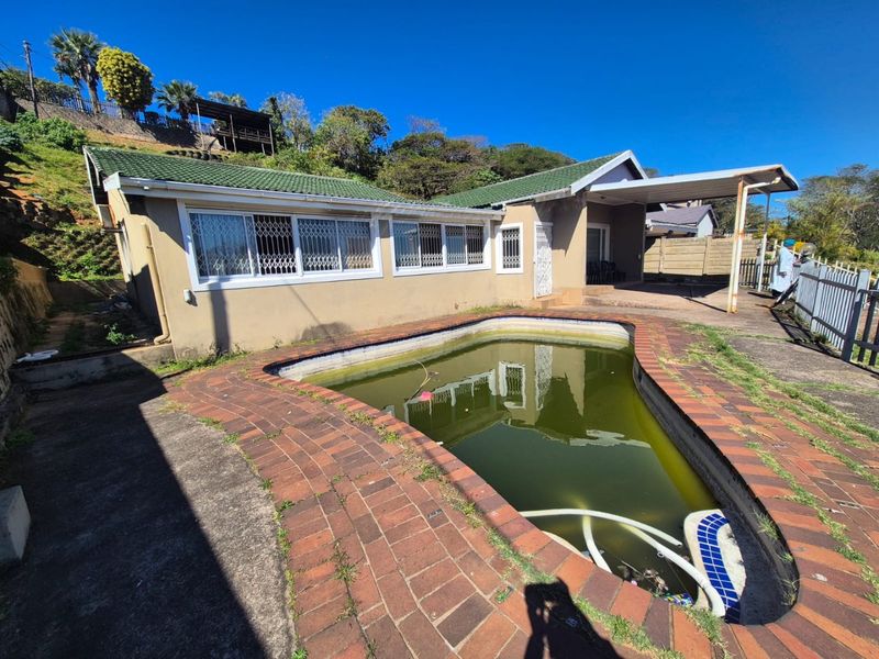 Rear exterior view featuring a swimming pool with stagnant water, brick paving, and a covered carport area attached to the main house structure.