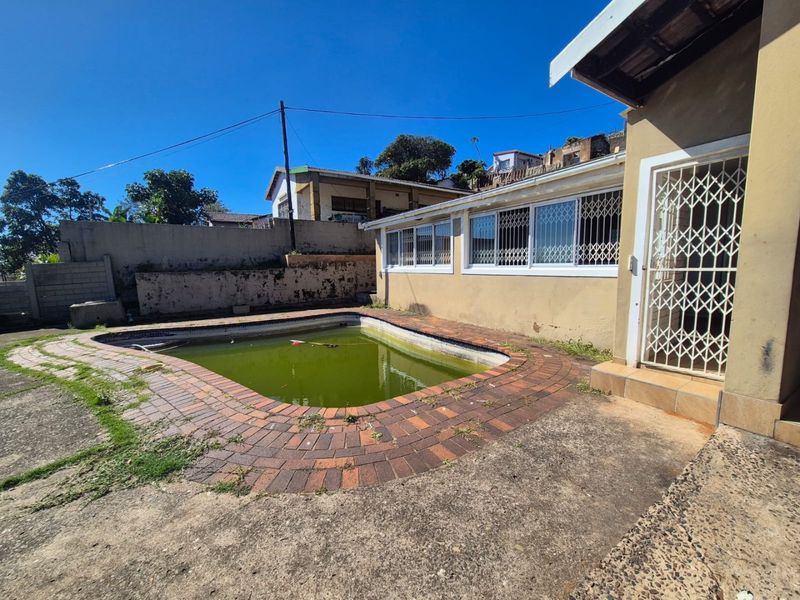 Outdoor pool area featuring a concrete patio, brick coping, and security-fitted windows, requiring significant maintenance and pool restoration.