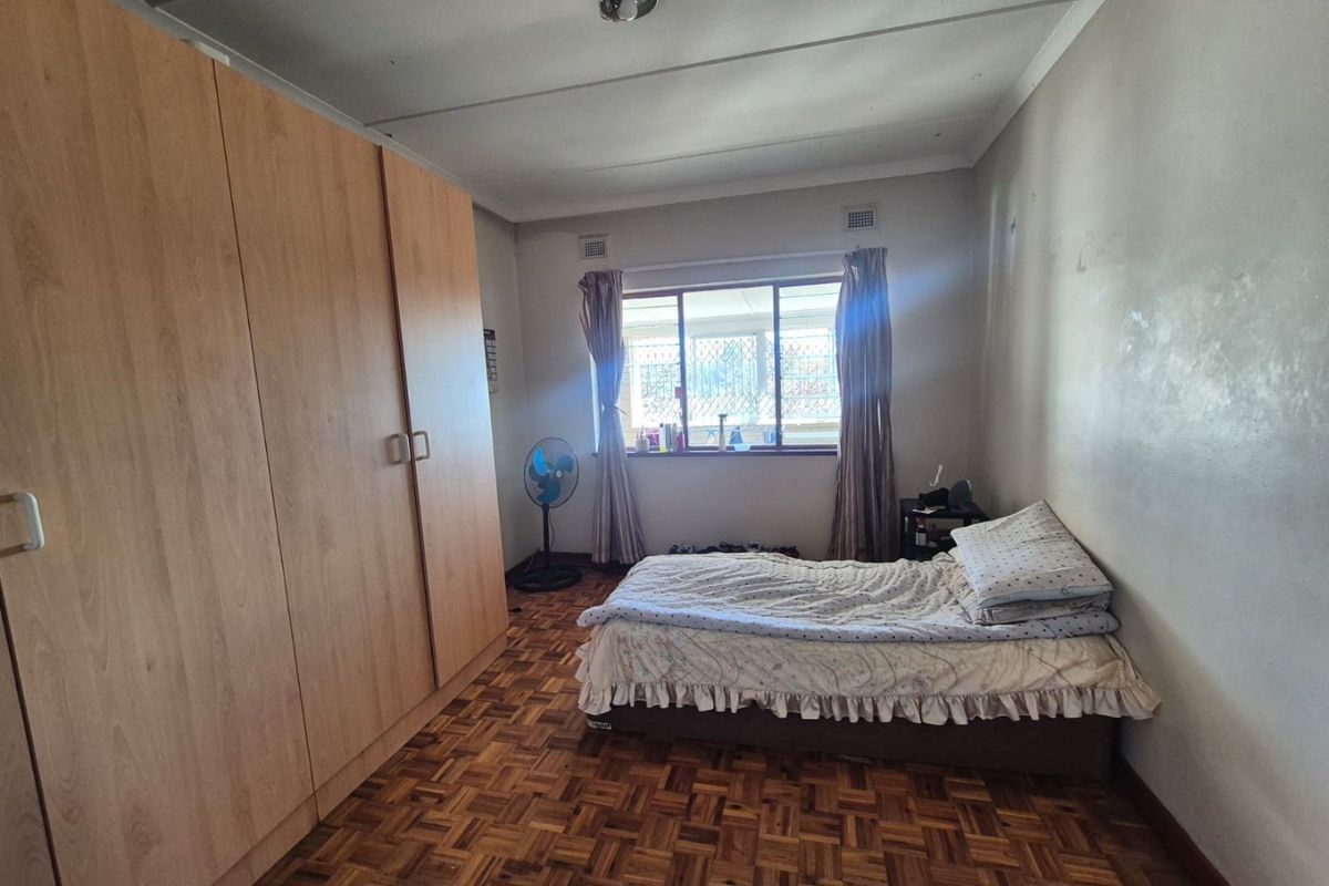 A bedroom featuring classic parquet flooring, a large built-in wardrobe, and a window fitted with security bars.