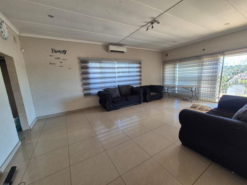 Spacious living room featuring neutral tiled flooring, a wall-mounted air conditioning unit, and large windows with modern roller blinds.