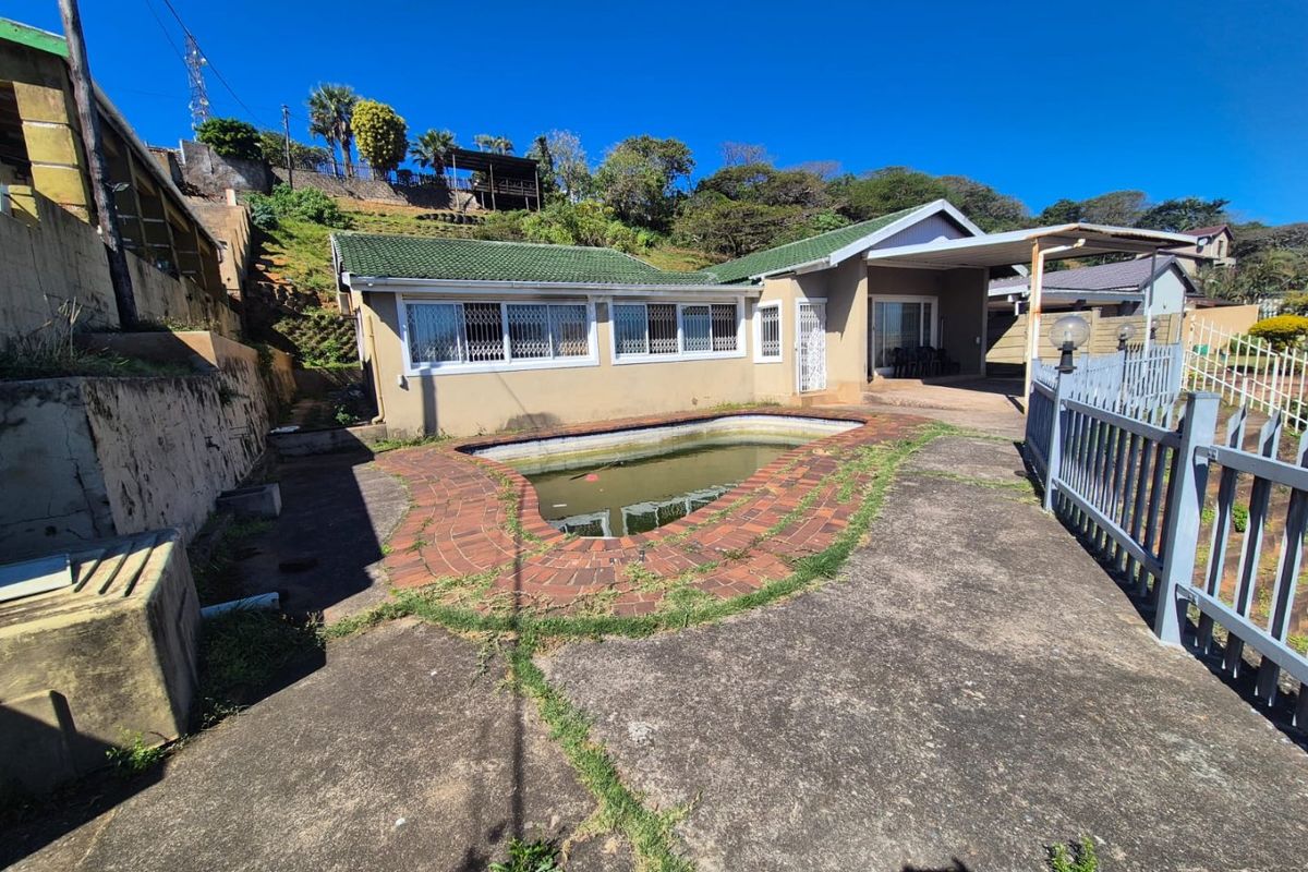 Rear exterior view of the house featuring a swimming pool, concrete patio area, and a carport, set against a sloped garden backdrop.