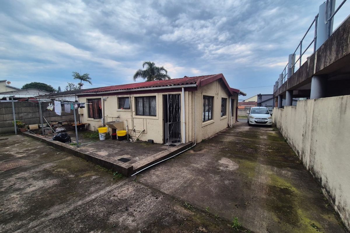 Rear exterior view of the property featuring a concrete driveway, patio area, and external wash basin, showing signs of weathering and maintenance requirements.