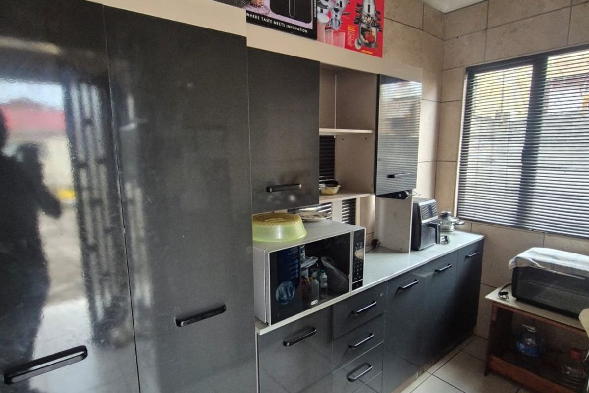 A functional kitchen featuring dark grey cabinetry, tiled flooring, and a window with fitted blinds, providing a clean and practical workspace.
