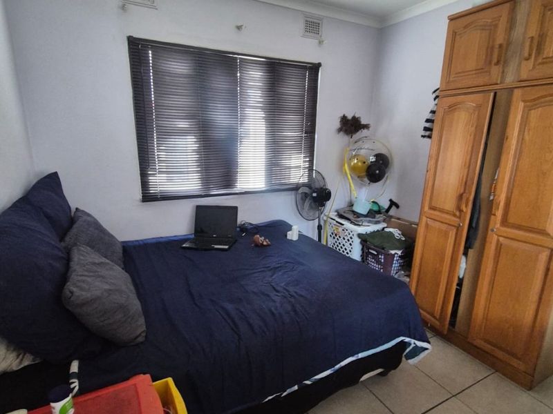 A functional bedroom featuring tiled flooring, a built-in wooden wardrobe, and venetian blinds on the window.