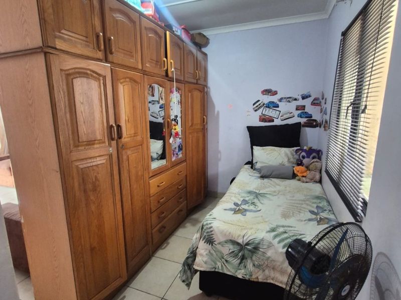 A compact bedroom featuring tiled flooring, a large built-in wooden wardrobe, and venetian blinds on the window.
