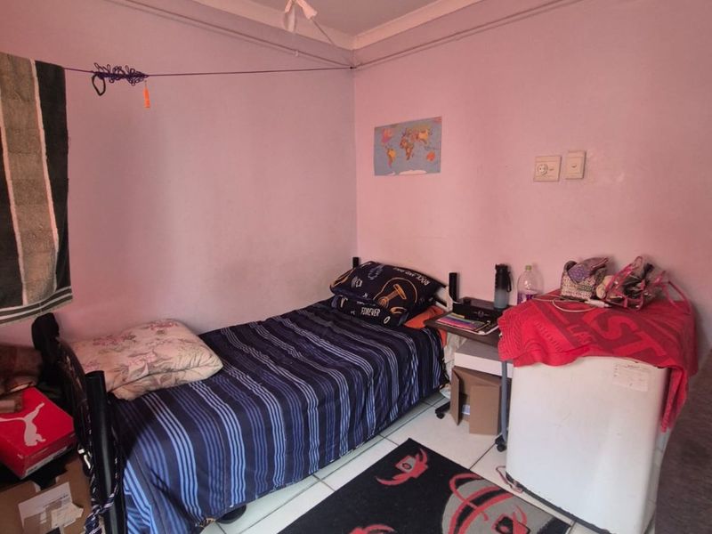 A compact bedroom featuring tiled flooring and basic electrical fixtures, currently used as a multi-purpose living space.