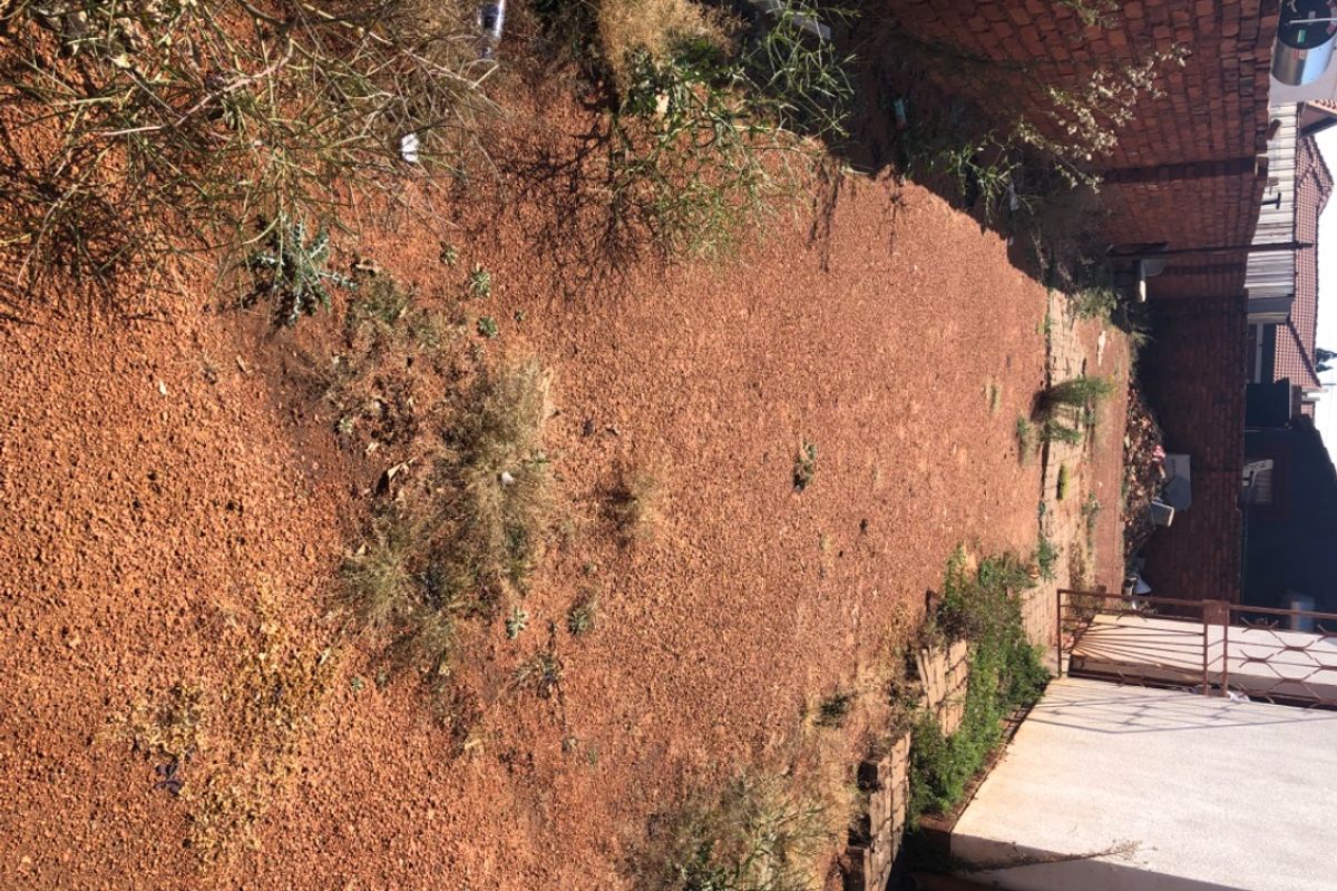 A vacant residential plot area featuring a dirt ground surface, enclosed by brick boundary walls and a metal gate.