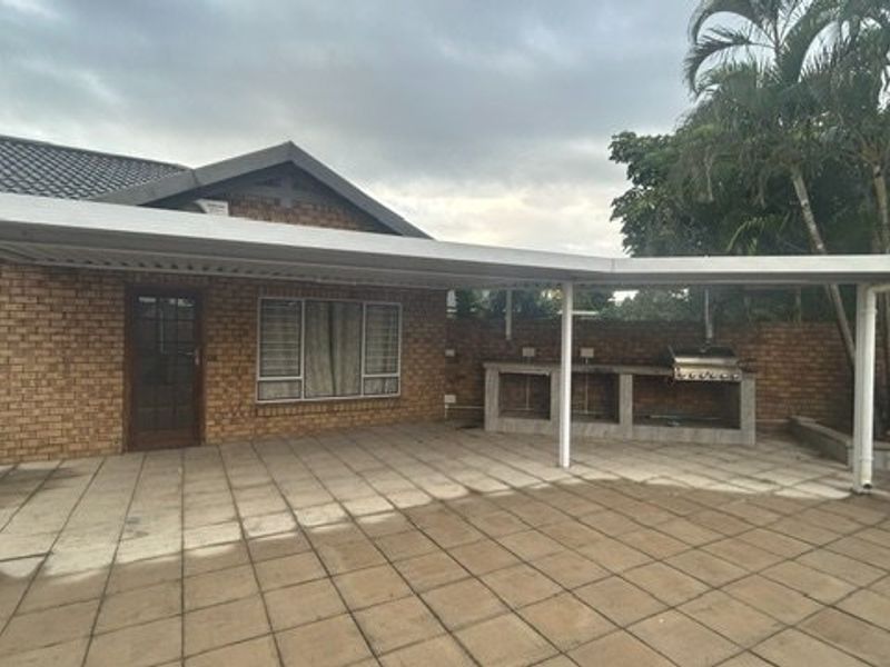 Spacious covered patio featuring paved flooring and a built-in braai area, perfect for outdoor entertaining against a classic brick facade.