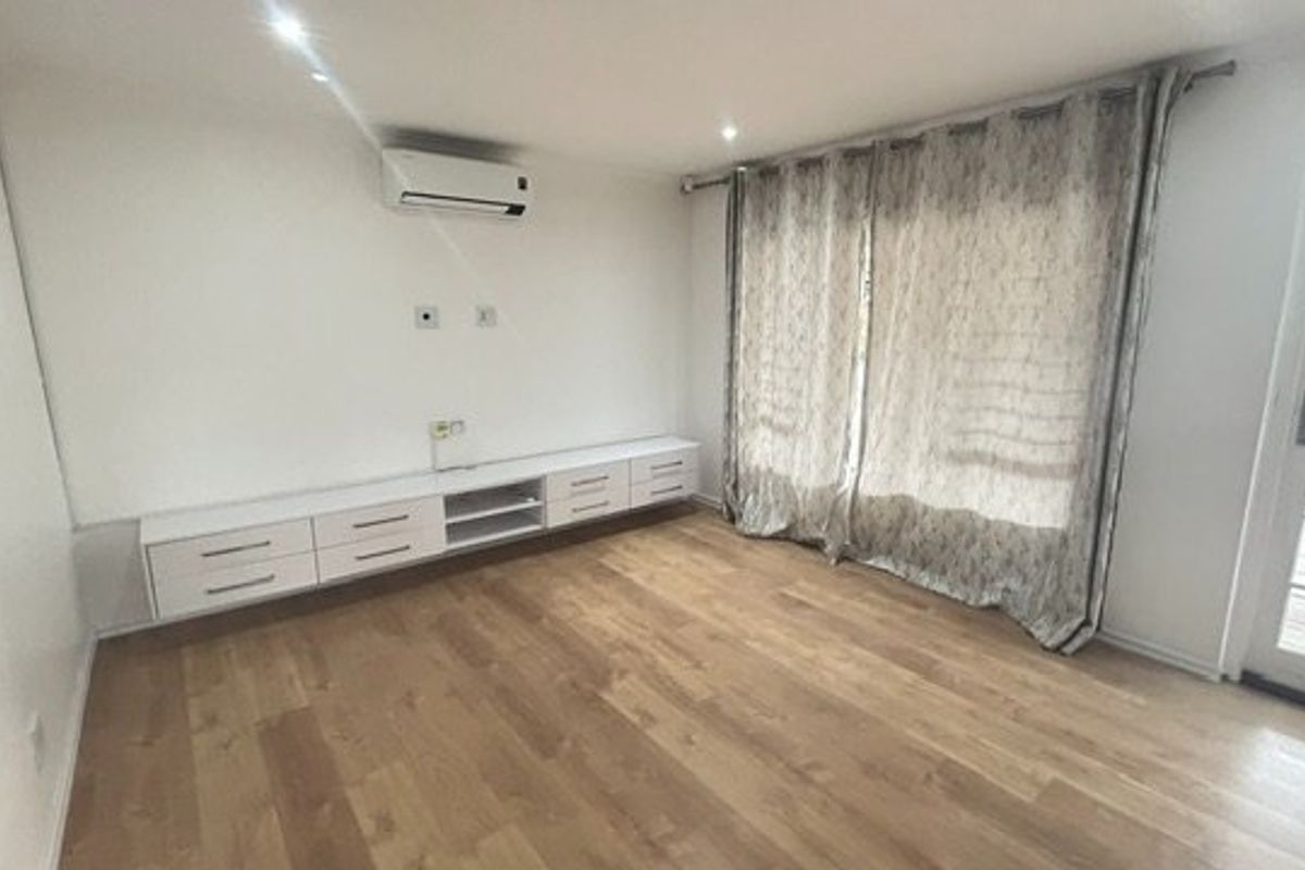 A bright, empty living room featuring modern laminate flooring, built-in cabinetry, a wall-mounted air conditioner, and direct access to an outdoor patio area.