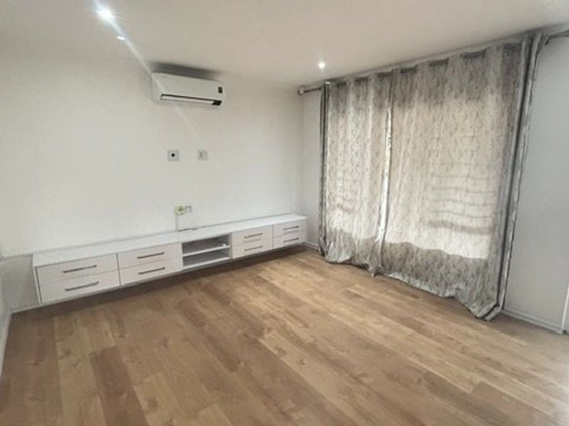 A bright, empty living room featuring modern laminate flooring, built-in cabinetry, a wall-mounted air conditioner, and direct access to an outdoor patio area.
