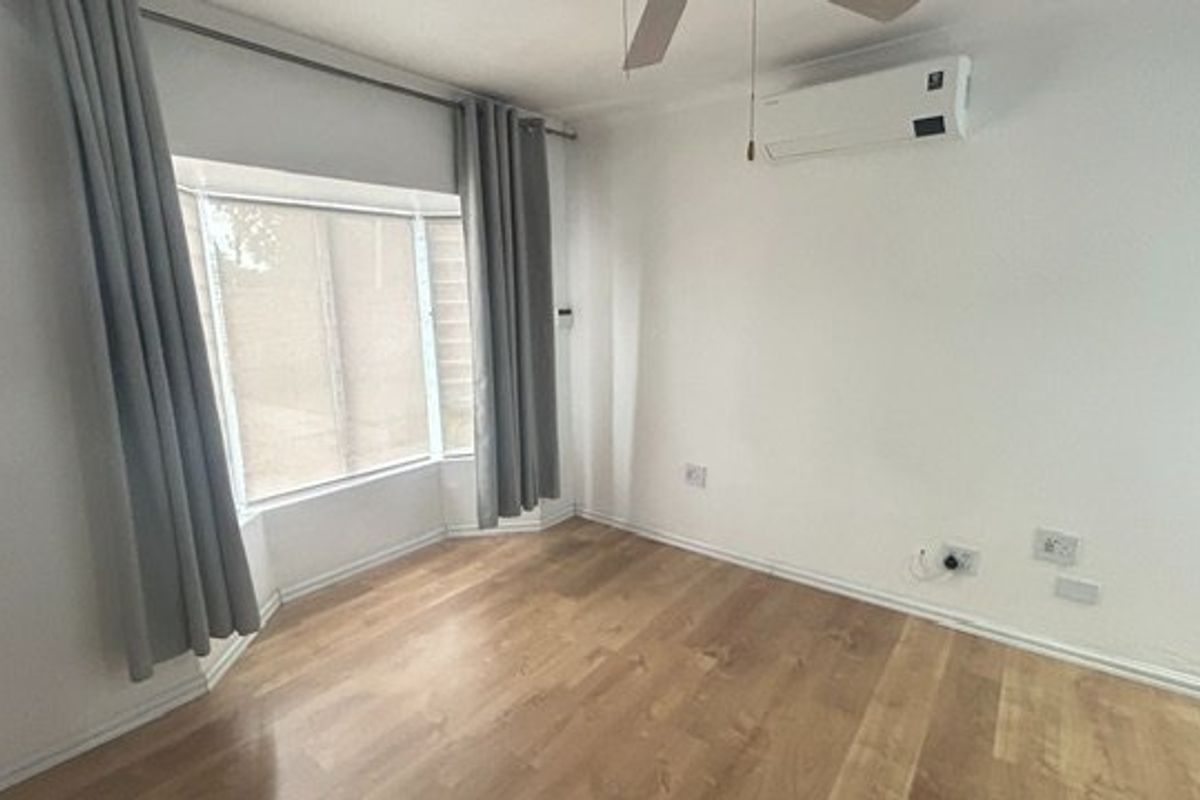 A bright, empty bedroom featuring laminate flooring, a bay window, a ceiling fan, and a wall-mounted split-system air conditioner.