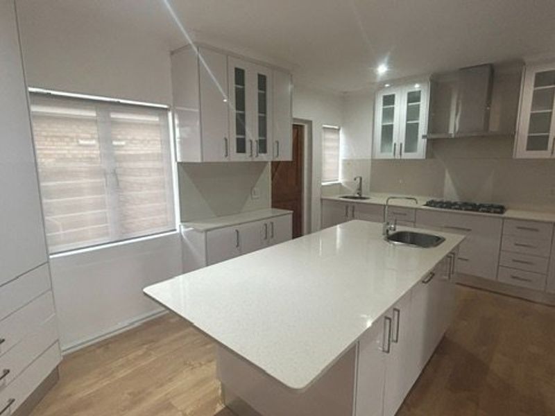Modern kitchen featuring high-gloss white cabinetry, quartz countertops, a central island with sink, built-in oven, gas hob, and integrated extractor fan.