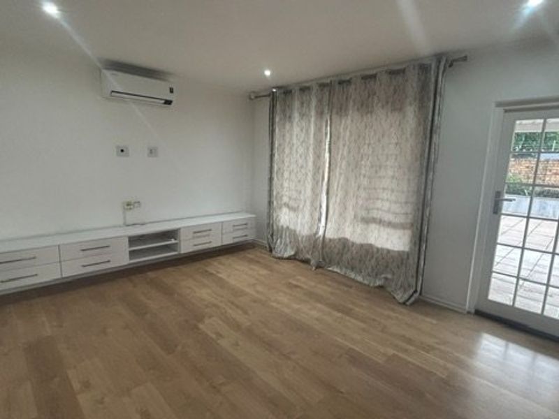 A bright, empty living room featuring laminate flooring, built-in cabinetry, a split-system air conditioner, and direct access to an outdoor patio area.