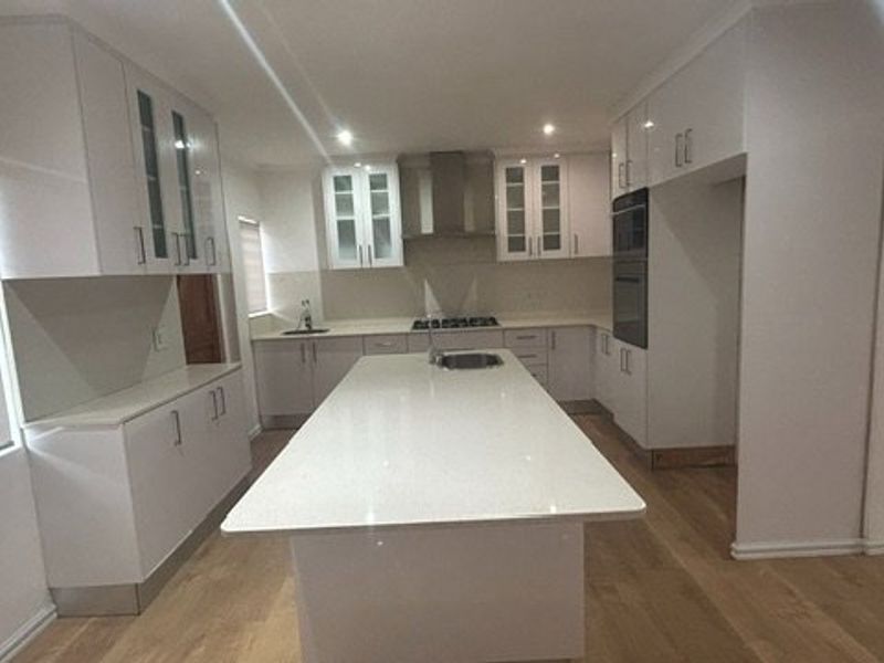 Modern kitchen featuring white cabinetry, a central island with quartz countertops, built-in oven, gas cooktop, and light wood-look flooring.